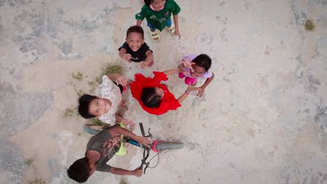 Niños-Felices-Mirando-Hacia-Arriba-Y-Agitando-Sus-Manos-Al-Dron-En-Berau,-Indonesia