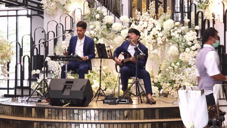 Dos-Cantantes-De-Bodas-Cantan-Y-Tocan-Sus-Instrumentos-Musicales,-Una-Guitarra-Y-Una-Batería-Digital-Para-Una-Recepción-De-Boda-En-Un-Hotel-De-Bangkok,-Tailandia.