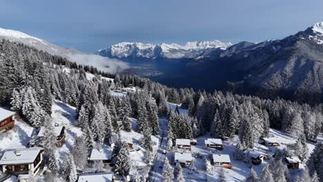 Drone-wide-shot-showing-small-swiss-village-on-snowy-mountain-with-icy-mountain-range-in-background-during-sunny-day---Chur,-Switzerland
