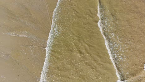 Aerial-footage-of-waves-gently-breaking-on-the-beach,-with-golden-sand