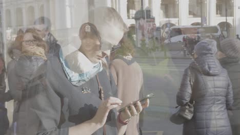 An-Einem-Sonnigen-Tag-Sieht-Man-Auf-Der-Straße-Im-Spiegelbild-Der-Vitrine-Ein-Junges-Mädchen,-Das-Mit-Dem-Handy-Arbeitet