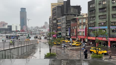 People-carry-umbrellas-and-walk-outside-Keelung-Railway-Station-on-a-rainy-day-and-against-the-background-of-a-street-in-Keelung-City,-Ren’ai-District,-Taiwan