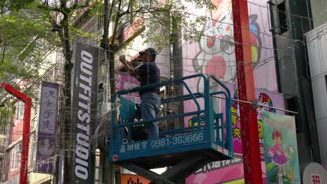 Escena-De-Un-Trabajador-Parado-En-La-Plataforma-De-Trabajo-Elevada-Móvil-Colocando-Decoraciones-De-Luces-Navideñas-En-Taipei-Ximending,-Taiwán