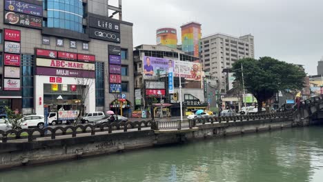 Panning-view-shot-of-the-Keelung-Tianliao-River-canal-against-the-background-of-MOYA-Sparkle-shopping-mall-in-Ren’ai-District,-Taiwan