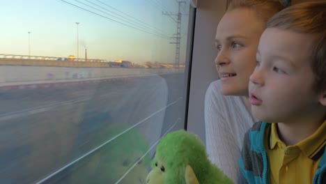 Small-boy-with-mother-sitting-against-window-in-their-rail-train-place-and-watching-outside