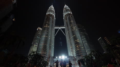 Zeitrafferansicht-Der-Petronas-Twin-Towers-Bei-Nacht-Vom-Boden-Aus-Mit-Menschen-In-Kuala-Lumpur,-Malaysia