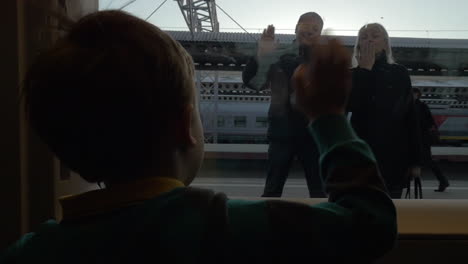 Slow-motion-view-of-boy-watching-in-window-from-rail-train-and-saying-goodbye-his-grandparents-swinging-arms