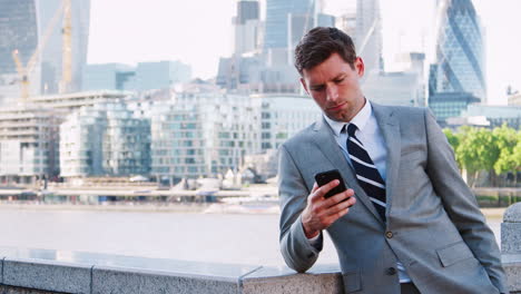 Businessman-Checking-Text-Messages-By-London-City-Skyline