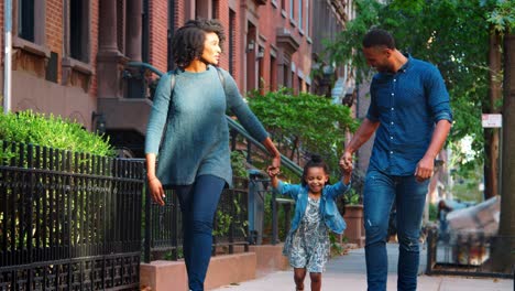Young-black-couple-swinging-daughter-as-they-walk-in-the-street