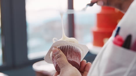 Woman-frosting-muffin-at-bakery-using-spatula,-mid-section