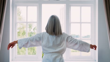 Senior-Woman-Opens-Curtains-And-Stretches-In-Front-Of-Window