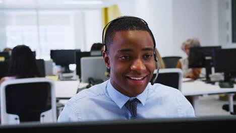 Young-man-working-at-computer-with-headset-in-busy-office