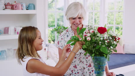 Senior-woman-and-granddaughter-arranging-flowers-in-kitchen