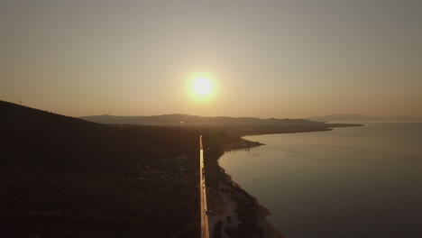 Flying-over-Trikorfo-Beach-shoreline-and-waterfront-road-at-sunset-Greece