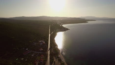 Volando-Sobre-El-Mar-Y-La-Costa-Con-La-Carretera-A-Lo-Largo-De-La-Playa-De-Trikorfo,-Grecia