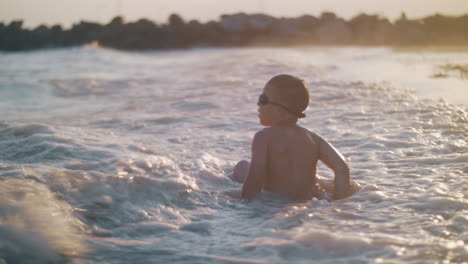 Kind-Badet-Im-Meer-Nahe-Der-Küste-Bei-Sonnenuntergang