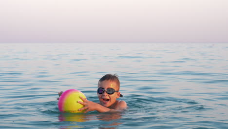 Glückliches-Kind,-Das-Mit-Ball-Im-Meer-Badet