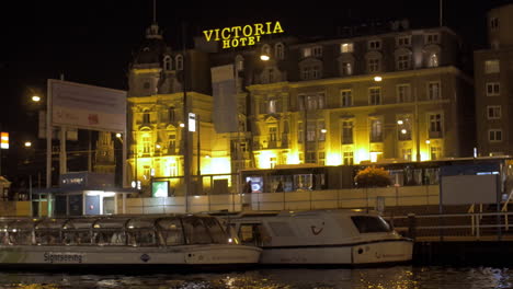 Blick-Auf-Victoria-Hotel-Und-Kanal-Mit-Touristischen-Booten-Amsterdam