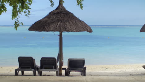 View-of-empty-chaise-longue-near-native-sun-umbrella-against-blue-water-Mauritius-Island