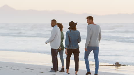 Rear-View-Of-Friends-Walking-Along-Winter-Beach-Together