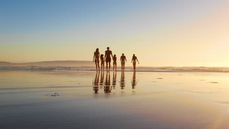 Friends-Walking-Towards-Waves-At-Sunset-On-Beach-Vacation
