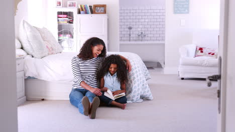 Young-mixed-race-mum-reading-book-with-daughter-in-her-room