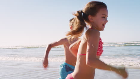 Niño-Y-Niña-En-Vacaciones-De-Verano-Corriendo-Por-La-Playa-Y-Saludando-Juntos