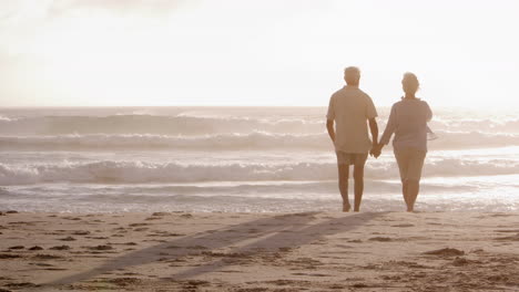 Rückansicht-Eines-Romantischen-älteren-Paares-Im-Sommerurlaub,-Das-Am-Strand-Entlang-Spaziert