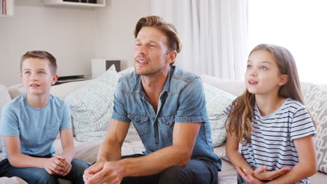 Father-And-Children-Sitting-On-Sofa-At-Home-Playing-Charades