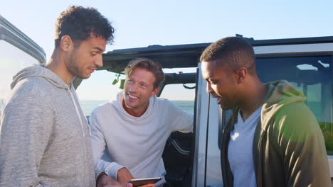 Three-young-men-using-tablet-computer-talking-by-their-car