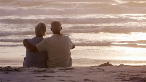 Rückansicht-Eines-älteren-Paares-Am-Strand,-Das-Den-Sonnenuntergang-über-Dem-Meer-Beobachtet