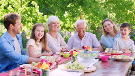Three-generation-family-at-lunch-in-garden-look-to-camera