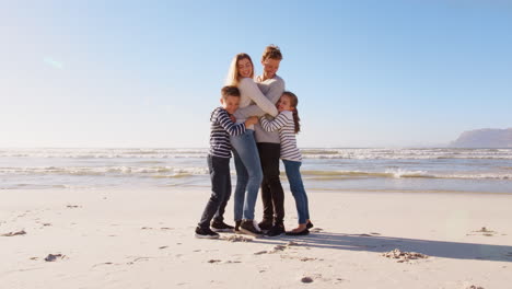 Children-Running-To-Embrace-Parents-As-They-Stand-On-Winter-Beach-Together