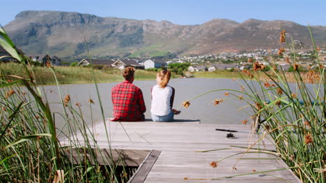 Couple-sitting-together-on-a-jetty-by-a-lake-talking