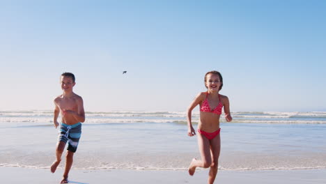 Junge-Und-Mädchen-Laufen-Im-Sommerurlaub-Gemeinsam-Am-Strand-Entlang-In-Richtung-Kamera