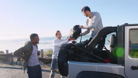 Three-young-adult-male-friends-unloading-backpacks-from-jeep