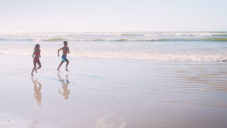 Junge-Und-Mädchen-Laufen-Im-Sommerurlaub-Gemeinsam-Am-Strand-Entlang-In-Richtung-Kamera