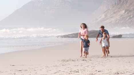 Parents-Chasing-Children-Along-Beach-On-Summer-Vacation