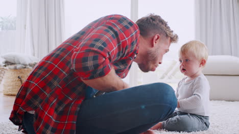 Dad-playing-ukulele-with-toddler-son-at-home,-side-view