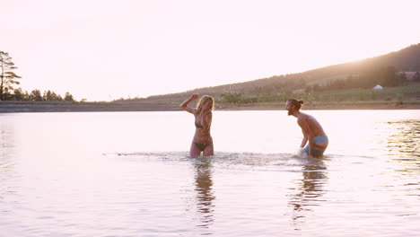 Couple-Having-Fun-Splashing-In-Lake-Backlit-By-Evening-Sun
