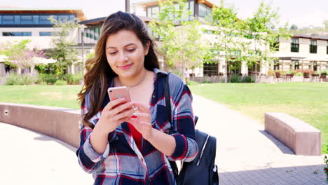 Female-High-School-Student-Checking-Messages-On-Mobile-Phone-Outside-College-Buildings