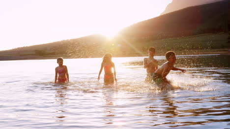 Group-Of-Children-Playing-And-Splashing-In-Lake-Backlit-By-Sun