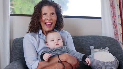 Grandmother-Sitting-On-Sofa-Playing-With-Baby-Grandson-At-Home