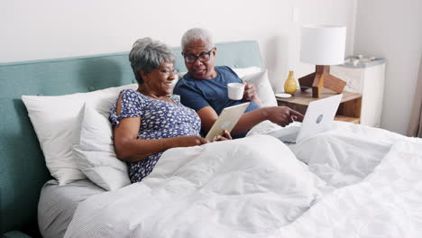 Älteres-Paar-Liegt-Im-Bett-Und-Nutzt-Digitale-Geräte