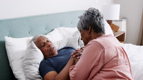 Senior-Woman-Comforting-Man-With-Illness-Lying-In-Bed-At-Home