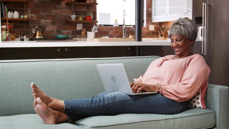 Senior-Woman-Relaxing-On-Sofa-At-Home-Using-Laptop-To-Shop-Online