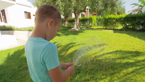 Playful-child-watering-green-lawn-by-the-house