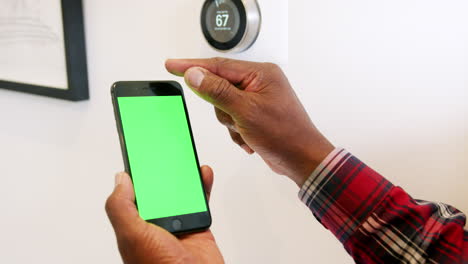 Close-Up-Of-Man-Setting-Smart-Heating-Thermostat-Using-Mobile-Phone-App