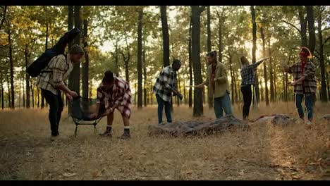 A-group-of-people-in-hiking-clothes-stop-for-a-break-and-arrange-their-things.-Stopping-and-resting-during-the-hike,-preparing-an-overnight-shelter-in-the-summer-forest.-A-group-of-people-in-plaid-shirts-stop-for-a-break