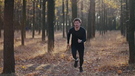 Close-up-shot-of-a-man-with-curly-hair-in-a-black-sports-uniform-running-quickly-during-his-morning-jog-in-the-autumn-forest-in-the-morning